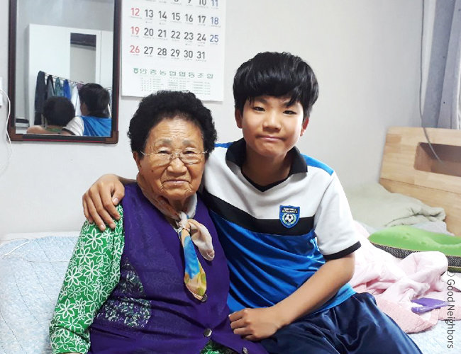 왼쪽은 좌측 냉장고와 우측 싱크대 사이에 밥솥, 상, 기타 주방 물품들이 쌓여 있는 부엌 겸 거실 사진, 오른쪽은 좌측부터 냉장고, TV, 에어컨이 지원되고 깔끔하게 정돈된 거실 사진